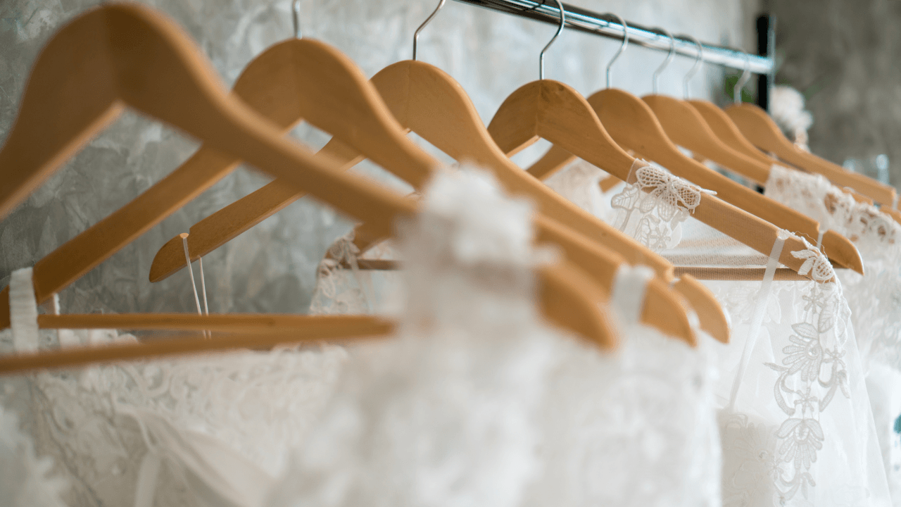 A few wedding dresses hanging on wooden hangers.