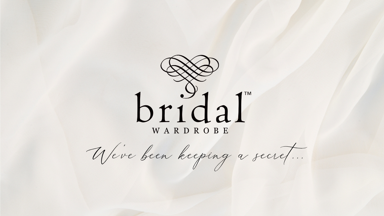 satin fabric with the bridal wardrobe logo on it saying "we've been keeing a secret"