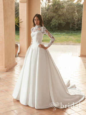 Bride wearing the ULANI Blue by Enzoani Mikado ballgown with a detachable high-neck long-sleeve jacket, princess-boned bodice, drop basque waist and cathedral train.