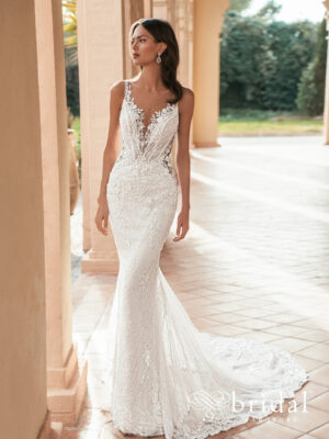 Bride wearing the ULARIA Blue by Enzoani column wedding dress with an illusion plunging V neckline, sleeveless beaded vine lace straps and sweep train.