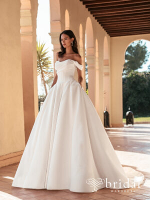 Bride wearing the ULIENNE Blue by Enzoani ballgown wedding dress with a sweetheart neckline, off-the-shoulder sleeves, ruched bodice, hidden pockets and royal train.