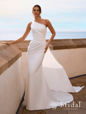 Bride wearing the FLYNNE column wedding dress from the Love collection with a one-shoulder neckline, sculpted ruching, open back, flowing cape and sweep train.